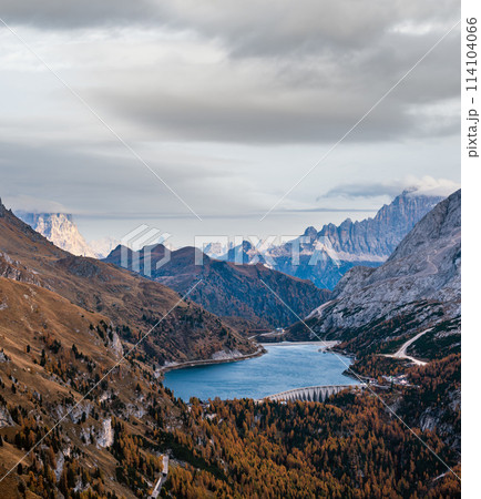 Autumn Dolomites mountain scene from hiking path betwen Pordoi Pass and Fedaia Lake, Italy. Snowy Marmolada Glacier and Fedaia Lake in far. Autumn Dolomites mountain scene from hiking path betwen Pordoi Pass and Fedaia Lake, Italy. Snowy Marmolada Glacier and Fedaia Lake in far. 114104066