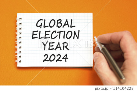 Global election year 2024 symbol. Concept words Global election year 2024 on beautiful white note. Beautiful orange background. Voter hand. Business Global election year 2024 concept. Copy space 114104228
