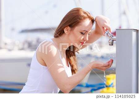 Woman drinking water from tap in marina. 114105025