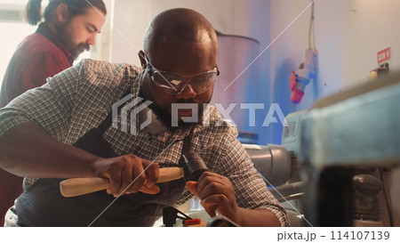 African american manufacturer shaping raw timber using chisel and hammer, creating wood art, making precise cuts. Artist making handmade wood sculptures, engraving lumber with tools, camera B close up 114107139