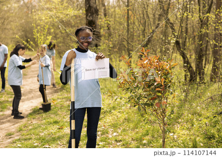 Portrait of african american girl holding banner with save our planet message, spreading ecological justice and awareness. Teenager activist posing with a poster to fight environmental pollution. 114107144