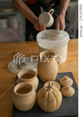 Close-up of a potter's hands glazing a ceramic mug. Vertical photo.  114107985