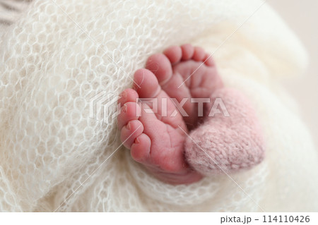 The tiny foot of a newborn baby. Soft feet of a new born in a white wool blanket. Close up of toes, heels and feet of a newborn. Knitted pink heart in the legs of a baby. Macro photography 114110426