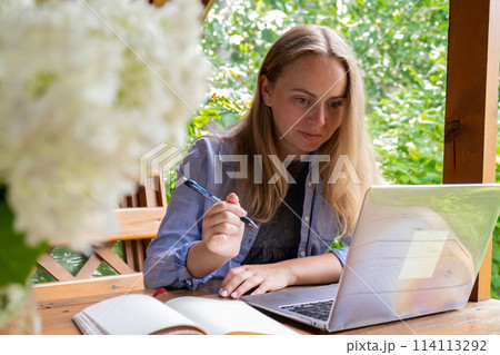 Female student has online lesson education outdoor in garden wooden alcove. Blonde woman sitting outside work on laptop having video call Female student has online lesson education outdoor in garden wooden alcove. Blonde woman sitting outside work on laptop having video call 114113292