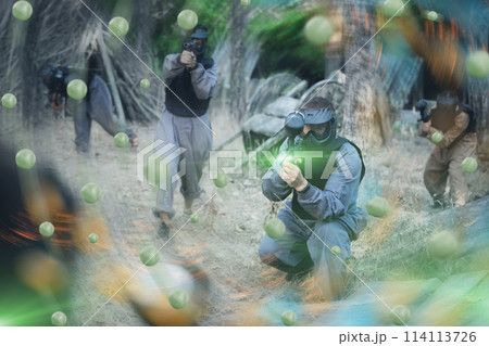 Team of positive smiling people playing paintball on battlefield outdoor, running with guns Team of positive smiling people playing paintball on battlefield outdoor, running with guns 114113726