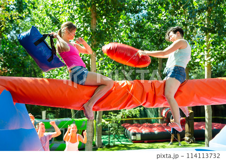 Women having pillow fight between each other in outdoor amusement park 114113732