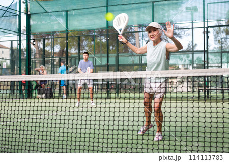 Senior woman playing padel tennis match during training on court 114113783
