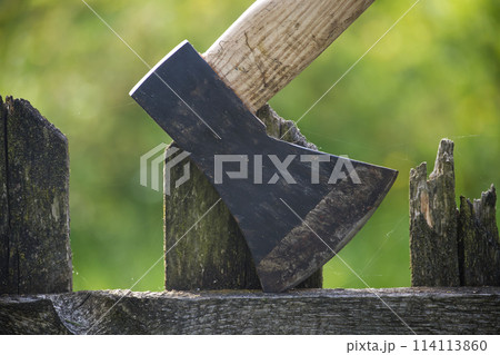 Detailed view of axe lodged into an old, weathered wooden fence 114113860