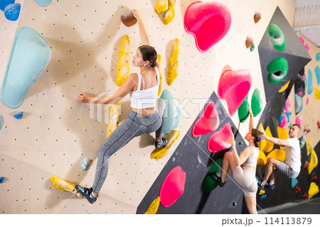 Motivated girl climbing without ropes on artificial bouldering wall 114113879