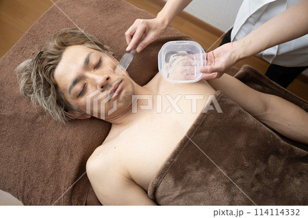 脱毛の施術を受ける男性の顔にジェルを塗る女性の手元 脱毛の施術を受ける男性の顔にジェルを塗る女性の手元 114114332