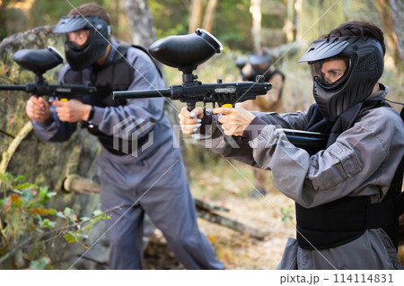 Paintball players aiming and shooting with guns at opposing team Paintball players aiming and shooting with guns at opposing team 114114831