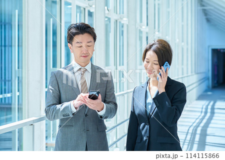 スマートフォンを操作するスーツ姿の男女 114115866