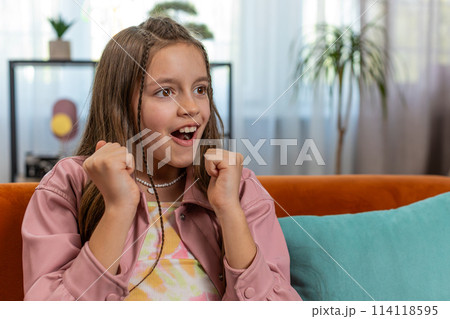 Happy girl child shouting celebrating win goal good news lottery luck victory watching TV at home 114118595