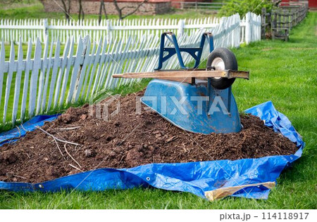 Wheelbarrow and pile of soil on a tarp in rural landscape picket fence Wheelbarrow and pile of soil on a tarp in rural landscape picket fence 114118917