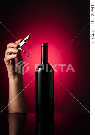 Unopened bottle of red wine and hands with corkscrew. 114120941