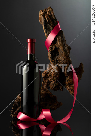 Bottle of red wine and old weathered snag with red satin ribbon. Bottle of red wine and old weathered snag with red satin ribbon. 114120957