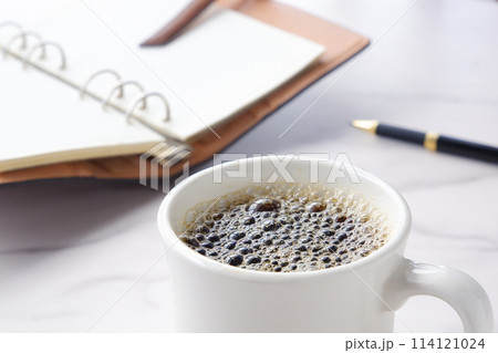 コーヒーを飲みながら、リング式のシステム手帳を開いて、仕事の段取りを考えているイメージ コーヒーを飲みながら、リング式のシステム手帳を開いて、仕事の段取りを考えているイメージ 114121024
