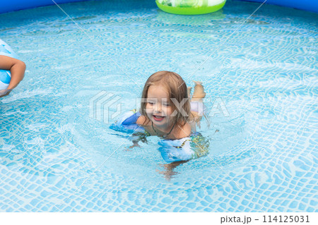 Children swim in an inflatable pool in the backyard of a house On a hot summer day children escape the heat in the cool water of an inflatable pool. Children have fun swimming in the inflatable pool. 114125031