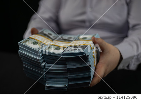 A businessman places stacks of dollars on the table in front of him. A man places stacks of hundred dollar bills on the table in front of him. Counting money on a black background. A businessman places stacks of dollars on the table in front of him. A man places stacks of hundred dollar bills on the table in front of him. Counting money on a black background. 114125090