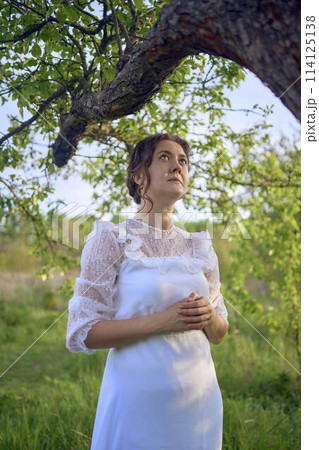 beautiful woman in white vintage dress with train in spring garden at sunset beautiful woman in white vintage dress with train in spring garden at sunset 114125138