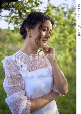 beautiful woman in white vintage dress with train in spring garden at sunset 114125139