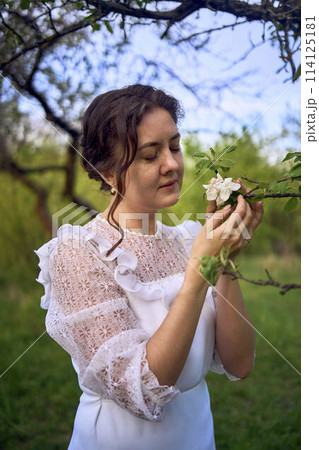 beautiful woman in white vintage dress with train in spring garden at sunset 114125181
