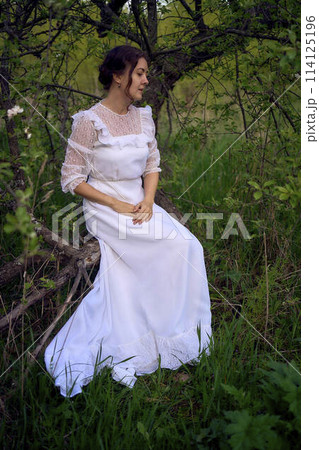 beautiful woman in white vintage dress with train in spring garden at sunset 114125196