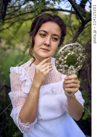beautiful woman in white vintage dress with train and holding vintage mirror in spring garden at sunset beautiful woman in white vintage dress with train and holding vintage mirror in spring garden at sunset 114125201