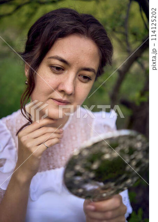 beautiful woman in white vintage dress with train and holding vintage mirror in spring garden at sunset beautiful woman in white vintage dress with train and holding vintage mirror in spring garden at sunset 114125202