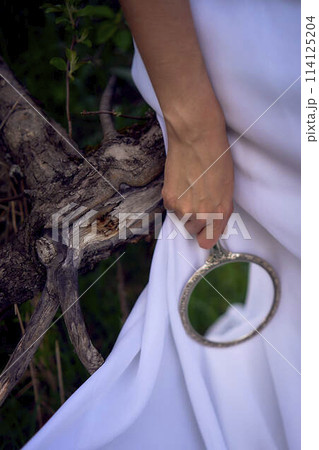 beautiful woman in white vintage dress with train and holding vintage mirror in spring garden at sunset beautiful woman in white vintage dress with train and holding vintage mirror in spring garden at sunset 114125204