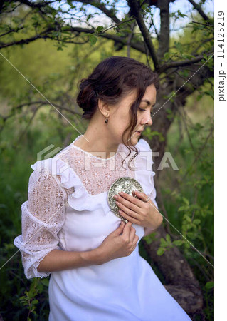 beautiful woman in white vintage dress with train and holding vintage mirror in spring garden at sunset beautiful woman in white vintage dress with train and holding vintage mirror in spring garden at sunset 114125219