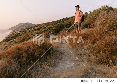 Traveler man with backpack walking on sea coastline with warm sun light. 114126122