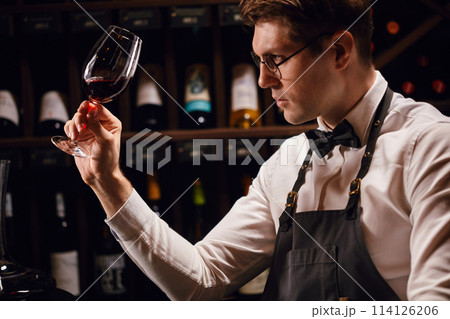 Professional sommelier holding a glass of delicious wine appreciting his tint Professional sommelier holding a glass of delicious wine appreciting his tint 114126206