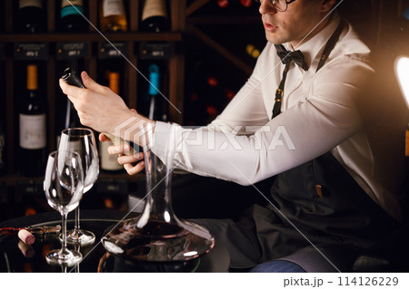 Elegant wine seller holding a bottle of wine and reading label in a wine store Elegant wine seller holding a bottle of wine and reading label in a wine store 114126229
