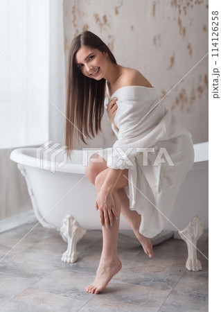 Young woman partially dressed in robe, taking care of her legs after having bath Young woman partially dressed in robe, taking care of her legs after having bath 114126258