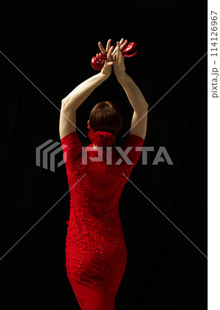 Moment frozen in time. Elegant woman in red dress standing with castanets against black background 114126967