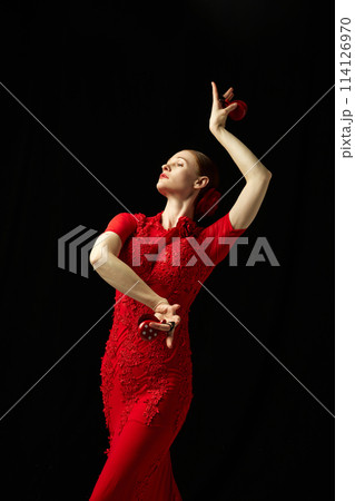 Elegant woman in beautiful red dress performing with castanets against black background. Following Spanish traditions Elegant woman in beautiful red dress performing with castanets against black background. Following Spanish traditions 114126970