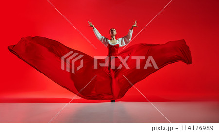 Passionate woman, flamenco dancer in stylish costume with skirt spreads like wings, performing against vivid red background 114126989