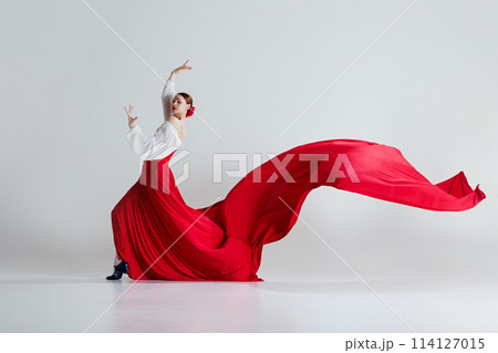 Passion. Female dancer in striking red costume performing flamenco dance against grey studio background. Breathtaking dance moment Passion. Female dancer in striking red costume performing flamenco dance against grey studio background. Breathtaking dance moment 114127015