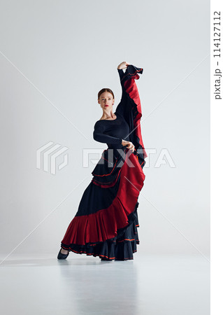 Elegance in motion. Skilled flamenco dancer, beautiful woman in expressive dress performing, dancing against grey studio background 114127112