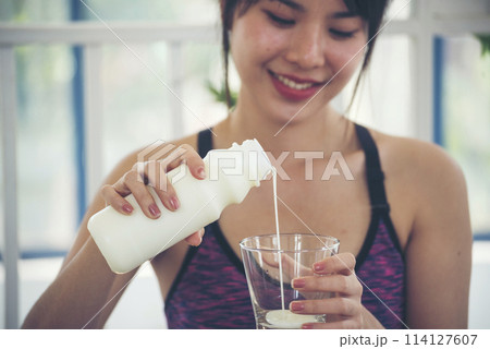 Women hands holding white glass of milk pouring from bottle. Asian women smile laugh look at camera health care home fitness lifestyle. Beautiful female drinking fresh milk low-fat dairy free lactose 114127607