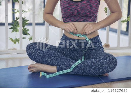Sport Women home fitness measure waist after workout exercise in living room. Close up Young woman hands using measurement tape in sportswear. Body weight traning healthy lifestyle diet concept Sport Women home fitness measure waist after workout exercise in living room. Close up Young woman hands using measurement tape in sportswear. Body weight traning healthy lifestyle diet concept 114127623