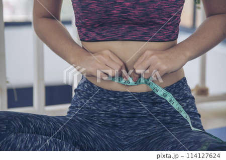 Sport Women home fitness measure waist after workout exercise in living room. Close up Young woman hands using measurement tape in sportswear. Body weight traning healthy lifestyle diet concept Sport Women home fitness measure waist after workout exercise in living room. Close up Young woman hands using measurement tape in sportswear. Body weight traning healthy lifestyle diet concept 114127624