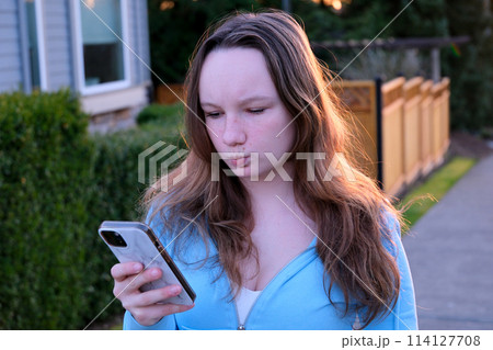 A beautiful girl in hoodie takes a selfie on her phone, pulls out her lips outdoors private sector in the city of Canada sunset backlight from behind A beautiful girl in hoodie takes a selfie on her phone, pulls out her lips outdoors private sector in the city of Canada sunset backlight from behind 114127708