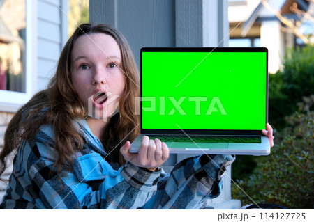 joy surprise girl holding laptop with green screen chroma key sitting teenager pointing fingers at screen advertising internet online entertainment sports interesting purchase everything for teen 114127725