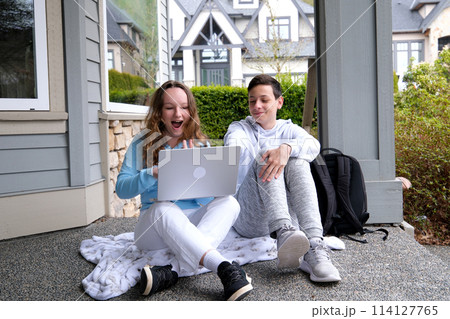 sit outside on porch whisper in ear have fun laugh doing homework boy and girl heterosexual friends teenager using laptop and tablet for online schooling from home together, quarantine concept. 114127765