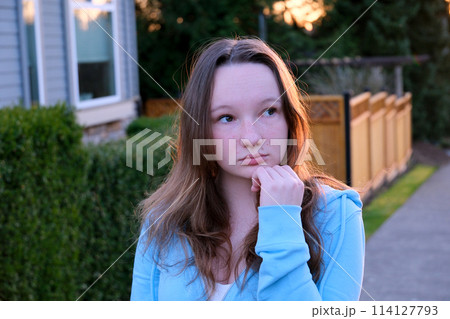 Portrait of a beautiful young girl looking into the camera and smiling. A charming woman dressed in a luxurious is standing on the street. 114127793