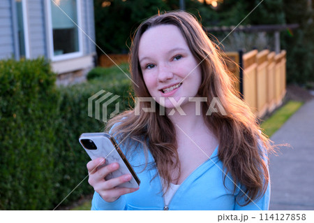 Portrait of happy hipster woman typing by mobile phone outdoors. Closeup cheerful girl walking with smartphone in urban background. Smiling lady holding cellphone in hands outside. 114127858