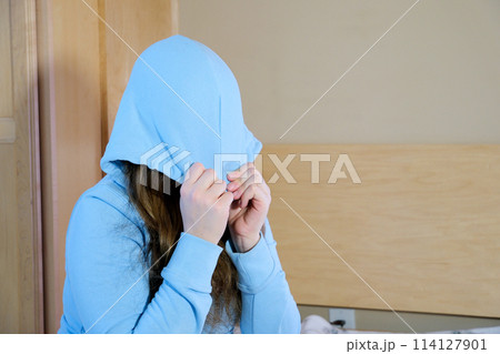 protest teenager girl teenager put a hood on her face pull a hood over her eyes in a room in the bedroom sitting alone sad crying suffering psychological problems of a child in adolescence 114127901