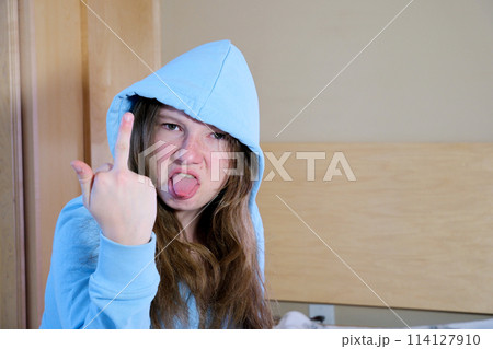 Young latin woman girl teenager hood on head stuck out tongue twisted face anger showing middle finger doing fuck you bad expression, provocation and rude attitude. screaming excited  114127910